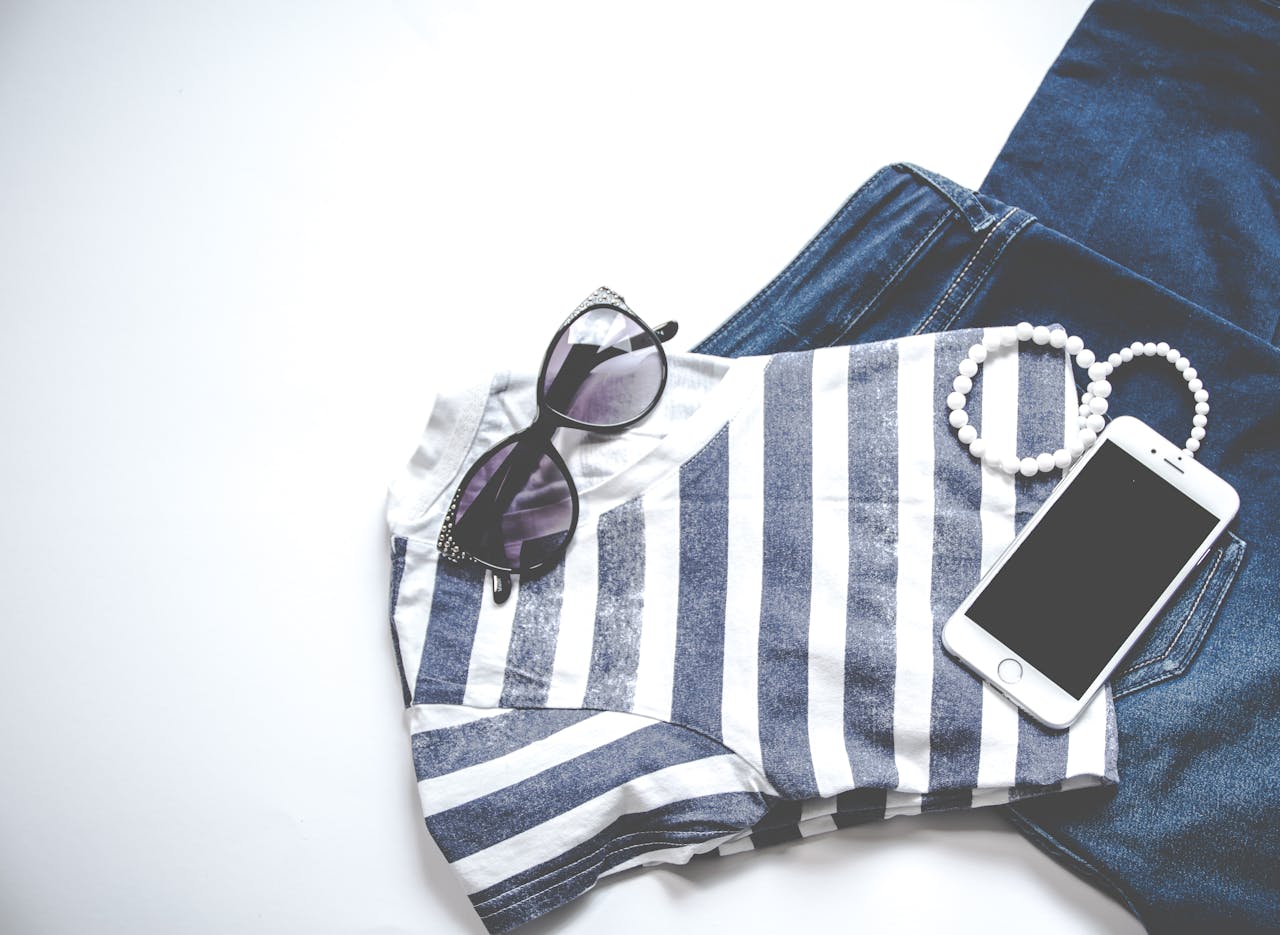 Home Flat lay image featuring sunglasses, striped top, jeans, and smartphone, ideal for fashion and lifestyle themes.